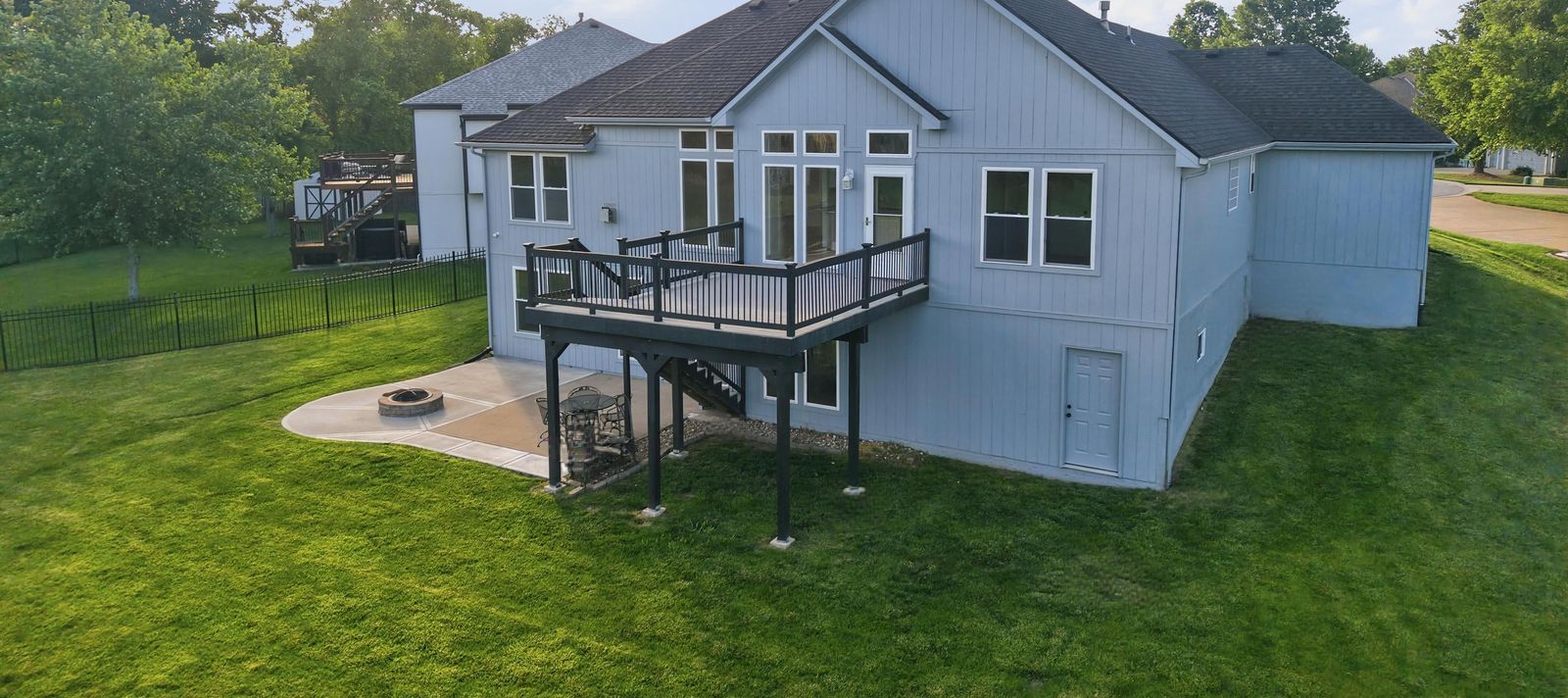 Aerial view of the back of a home with a deck and fire pit