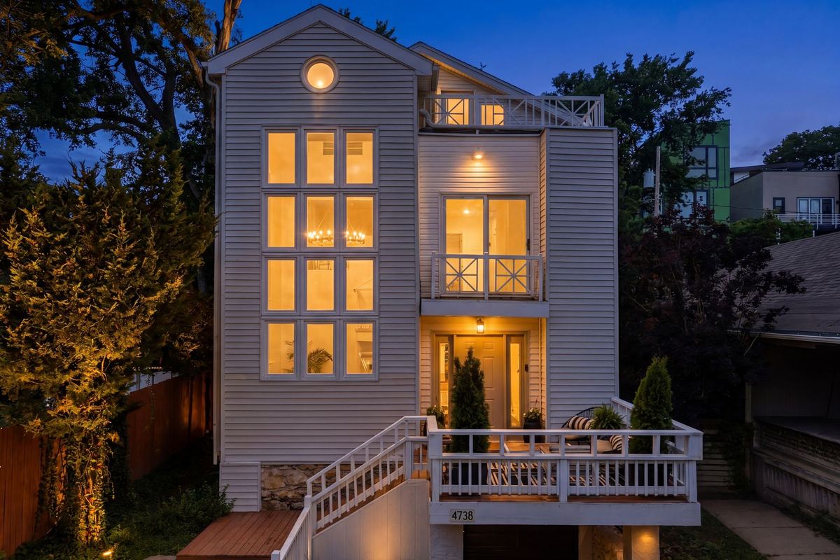 Three-story home at dusk with every window glowing, a virtual twilight edit