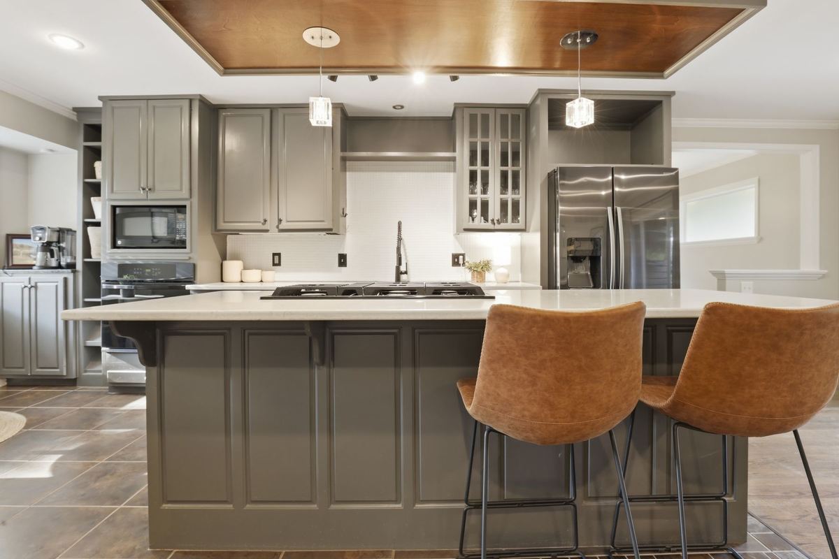 Kitchen with gray cabinets, a large island and leather bar stools